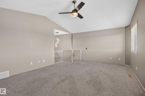 Spacious room featuring vaulted ceilings, a ceiling fan with integrated lighting, textured carpeting, and neutral wall tones - 13406 32A Street, Edmonton, AB 