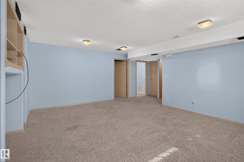 Spacious carpeted room featuring light blue walls, built-in shelving, multiple flush-mount light fixtures, and several interior doors - 13406 32A Street, Edmonton, AB 