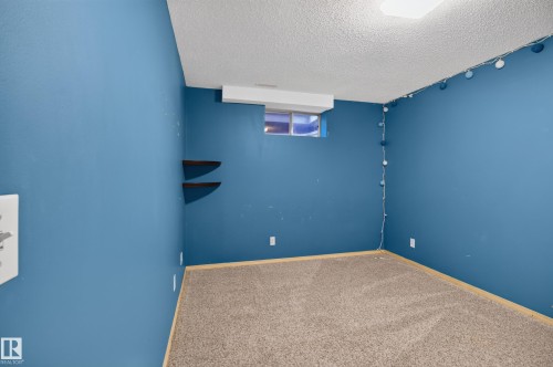Spacious room featuring blue-painted walls, textured ceiling, light brown carpet, and a window opening - 13406 32A Street, Edmonton, AB 