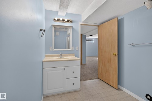 Bathroom featuring a single vanity with a countertop, integrated sink, and white cabinetry - 13406 32A Street, Edmonton, AB 