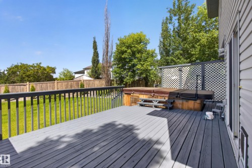 Spacious outdoor deck with a dark grey finish, featuring an integrated hot tub with wooden surround, and a white lattice privacy screen - 13406 32A Street, Edmonton, AB 