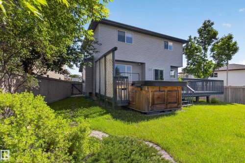 Spacious backyard featuring a two-story residence with gray siding, an expansive multi-level deck, and a built-in hot tub - 13406 32A Street, Edmonton, AB 