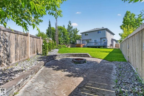 Expansive backyard featuring a stamped concrete patio with a built-in fire pit, a stone retaining wall, and a large manicured lawn - 13406 32A Street, Edmonton, AB 