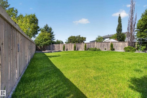 Expansive backyard featuring a large green lawn, full wood fencing, and mature perimeter trees - 13406 32A Street, Edmonton, AB 