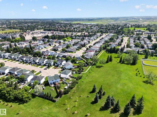 Expansive green space featuring mature evergreen trees and a paved walking path bordering residential properties - 13406 32A Street, Edmonton, AB 