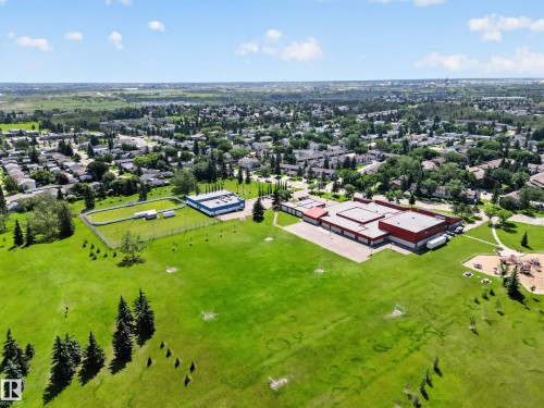 Expansive green space featuring mature trees, a fenced oval track, and a building with a blue facade - 13406 32A Street, Edmonton, AB 