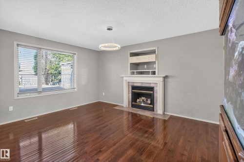 Spacious room featuring wood-finish flooring, a contemporary chandelier, and a fireplace with a tiled surround and mantel - 13406 32A Street, Edmonton, AB 
