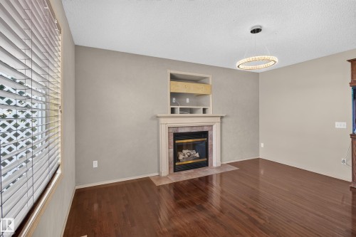 Living area featuring a fireplace with a stone surround and mantel, built-in shelving, wood-finish flooring, and a modern circular chandelier - 13406 32A Street, Edmonton, AB 