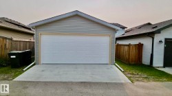 Detached garage featuring light gray siding, a white panel garage door, a concrete driveway, and a shingled roof - 