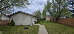 Expansive backyard featuring a manicured lawn, established trees, and a concrete pathway - 