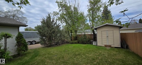 Expansive backyard featuring a green lawn, mature trees, a privacy fence, a storage shed, and a paved side yard - 4734 54A Avenue, Vegreville, AB - Outdoor