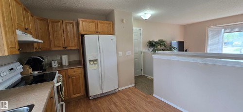 Kitchen featuring light wood cabinetry, laminate countertops, a built-in range hood, and a white side-by-side refrigerator - 4734 54A Avenue, Vegreville, AB - Indoor Photo Showing Kitchen