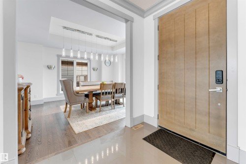 Entryway featuring a natural-finish paneled front door with smart lock hardware, tile flooring, and a cased opening leading to a dining area - 656 180 Street Sw, Edmonton, AB - Indoor