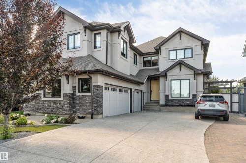 Modern stucco exterior featuring stone accents, a multi-gabled roofline, a two-car garage, and a concrete driveway - 656 180 Street Sw, Edmonton, AB - Outdoor With Facade