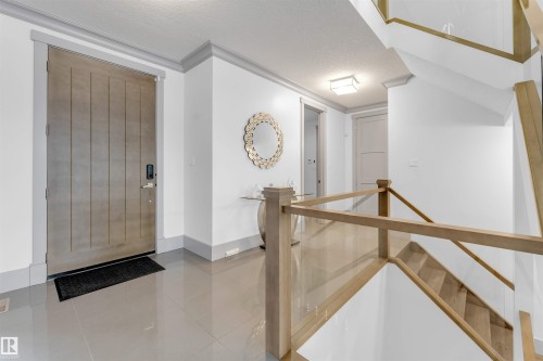 Bright entry foyer featuring large format tile flooring, a sleek wood-panel door, and a contemporary glass and wood railing staircase - 656 180 Street Sw, Edmonton, AB - Indoor Photo Showing Other Room