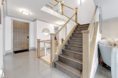 Contemporary interior featuring a wood-panel entry door, light grey tile flooring, and a staircase with wood treads and glass railings - 656 180 Street Sw, Edmonton, AB - Indoor Photo Showing Other Room