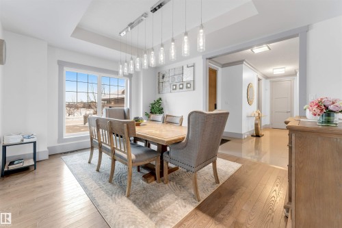 Spacious dining area featuring wood-finish flooring, a contemporary linear chandelier, tray ceiling detail, large picture windows, and an open archway to a tiled hallway - 656 180 Street Sw, Edmonton, AB - Indoor Photo Showing Dining Room