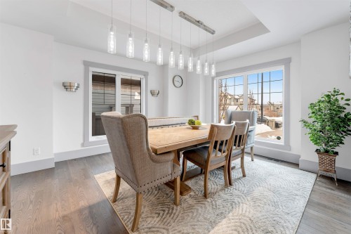 Dining area featuring dark wood-finish flooring, recessed ceiling with a linear pendant light fixture, large windows with grid patterns, and contemporary wall sconces - 656 180 Street Sw, Edmonton, AB - Indoor Photo Showing Dining Room