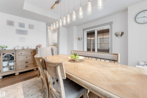 Dining area featuring a wood-finish dining table and chairs, a contemporary linear chandelier with multiple pendant lights, and hard-surface flooring - 656 180 Street Sw, Edmonton, AB - Indoor Photo Showing Dining Room