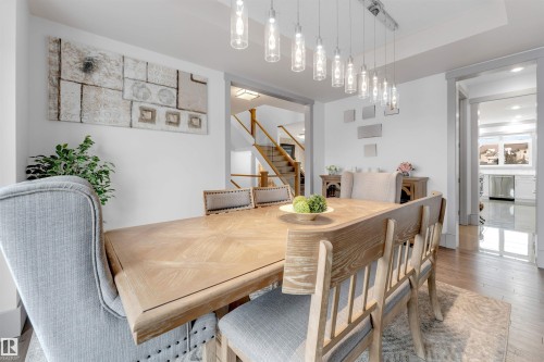 Dining area featuring a contemporary linear chandelier with multiple pendant lights, wood-finish flooring, and a broad doorway leading into another room - 656 180 Street Sw, Edmonton, AB - Indoor Photo Showing Dining Room