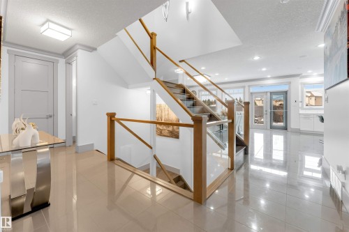 Grand entry featuring a multi-level staircase with wood railings and clear panel inserts, tile flooring, recessed lighting, and a transom window above the glass-paneled exterior door - 656 180 Street Sw, Edmonton, AB - Indoor Photo Showing Other Room