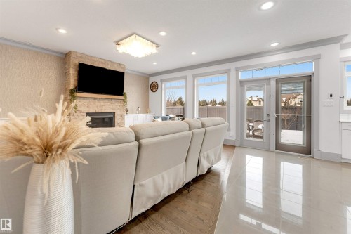 Living area featuring a stone-clad fireplace with a wood mantel, recessed lighting, and a contemporary ceiling fixture - 656 180 Street Sw, Edmonton, AB - Indoor Photo Showing Living Room With Fireplace