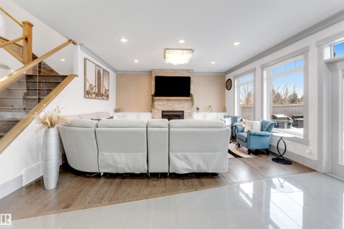Spacious living area featuring a stone-clad fireplace, wood-finish flooring, recessed lighting, and a contemporary chandelier - 656 180 Street Sw, Edmonton, AB - Indoor With Fireplace