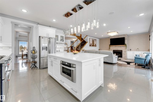 Open-concept kitchen featuring a large central island with integrated microwave, ample white cabinetry, stainless steel appliances, and large format tile flooring - 656 180 Street Sw, Edmonton, AB - Indoor Photo Showing Kitchen With Upgraded Kitchen