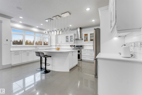 Spacious kitchen featuring an expansive central island with seating, a suite of stainless steel appliances, extensive white cabinetry, recessed lighting, and large windows - 656 180 Street Sw, Edmonton, AB - Indoor Photo Showing Kitchen With Upgraded Kitchen
