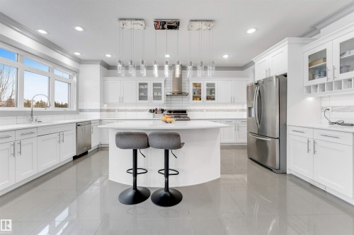Bright kitchen featuring an expansive center island with seating, white shaker cabinetry, stainless steel appliances, and a tiled backsplash - 656 180 Street Sw, Edmonton, AB - Indoor Photo Showing Kitchen With Upgraded Kitchen