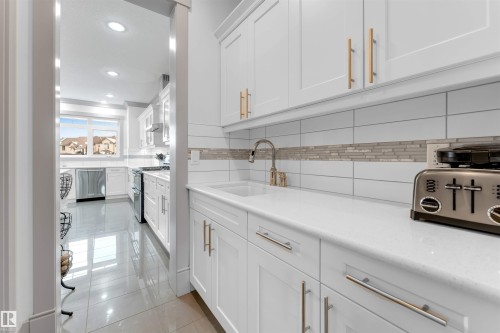 Bright kitchen prep area featuring shaker-style cabinetry, quartz countertops, a tile backsplash with a mosaic accent, and a built-in sink with a gooseneck faucet - 656 180 Street Sw, Edmonton, AB - Indoor Photo Showing Kitchen With Upgraded Kitchen