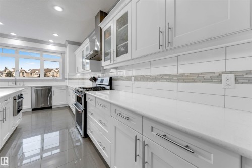Contemporary kitchen featuring white cabinetry, stainless steel appliances, a white tile backsplash with mosaic accent, and polished dark tile flooring - 656 180 Street Sw, Edmonton, AB - Indoor Photo Showing Kitchen With Upgraded Kitchen