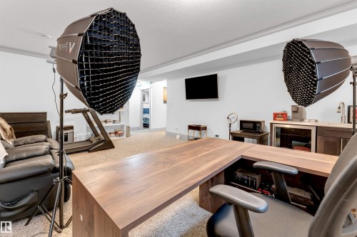 Built-in wood-finish desk with storage, wall-mounted television, and integrated wet bar featuring a sink - 656 180 Street Sw, Edmonton, AB - Indoor