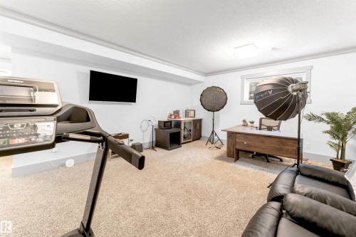 Spacious room featuring neutral carpet flooring, recessed lighting, a window with white trim, and a wall-mounted television - 656 180 Street Sw, Edmonton, AB - Indoor