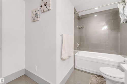 Bathroom featuring a white bathtub, glossy gray wall tiles, chrome fixtures, and coordinating gray floor tiles - 656 180 Street Sw, Edmonton, AB - Indoor Photo Showing Bathroom