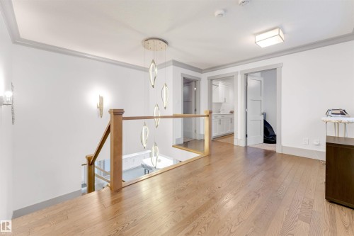 Hardwood flooring throughout a bright landing area, featuring a contemporary chandelier, recessed lighting, and a wood railing with glass paneling overlooking the lower level - 656 180 Street Sw, Edmonton, AB - Indoor Photo Showing Other Room