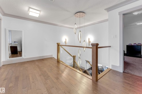 Upper-level landing featuring wood-finish flooring, a contemporary chandelier, a glass and wood-tone railing, wall sconces, and crown molding - 656 180 Street Sw, Edmonton, AB - Indoor Photo Showing Other Room