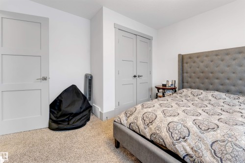 Carpeted room featuring a white interior door with brushed nickel hardware, a pair of light gray bifold closet doors, and contrasting gray baseboards and door trim - 656 180 Street Sw, Edmonton, AB - Indoor Photo Showing Bedroom