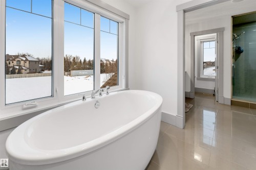 Freestanding oval bathtub with polished chrome fixtures, set against large white-framed windows - 656 180 Street Sw, Edmonton, AB - Indoor Photo Showing Bathroom