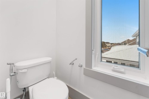 Bathroom featuring a white toilet, chrome bidet attachment, and a window with white trim - 656 180 Street Sw, Edmonton, AB - Indoor Photo Showing Bathroom