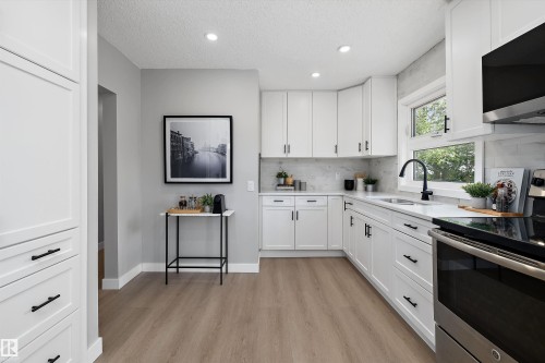 Modern kitchen featuring white shaker cabinetry, wood-finish flooring, a stainless steel range, and a black gooseneck faucet - 12912 103 Street, Edmonton, AB 