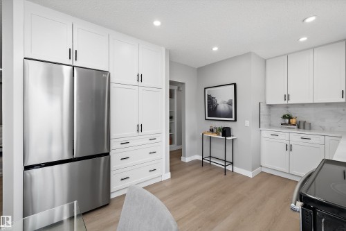 Modern kitchen featuring white shaker cabinetry with black hardware, stainless steel refrigerator, light wood-finish flooring, and recessed lighting - 12912 103 Street, Edmonton, AB 