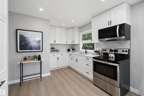 Modern kitchen featuring white shaker cabinetry, stainless steel appliances, wood-finish flooring, recessed lighting, and a white countertop with a corner sink - 12912 103 Street, Edmonton, AB 