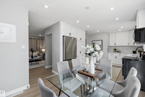 Open-concept living space featuring wood-finish flooring, recessed lighting, and a kitchen with white cabinetry, stainless steel refrigerator, and marble-look backsplash - 12912 103 Street, Edmonton, AB 