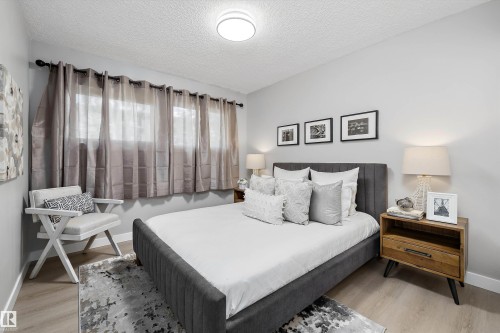 Light wood-finish flooring complements neutral wall tones in this bedroom featuring a window with sheer and blackout drapery - 12912 103 Street, Edmonton, AB 