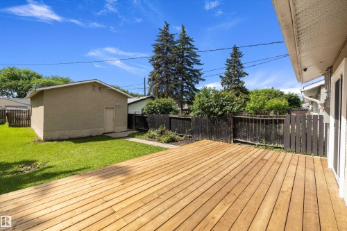 Expansive wood-finish deck with a private backyard, featuring a detached stucco garage, mature trees, and a dark-stained privacy fence - 12912 103 Street, Edmonton, AB 