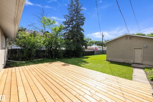 Expansive wooden deck with a spacious lawn area, mature trees, and a detached structure featuring a side entry door - 12912 103 Street, Edmonton, AB 