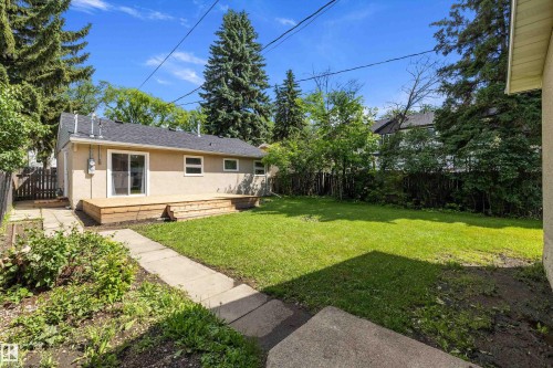 Expansive backyard featuring a large green lawn, a multi-tiered wood deck, a sliding glass door entry, and mature perimeter trees - 12912 103 Street, Edmonton, AB 