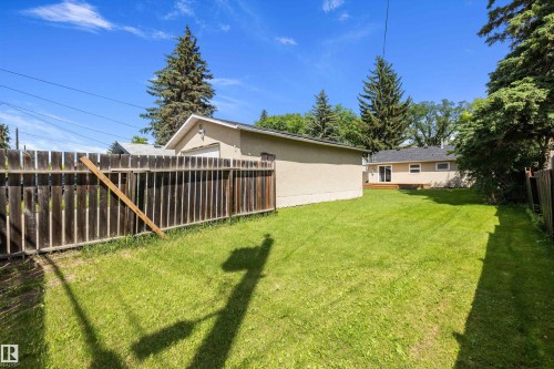 Expansive backyard featuring a manicured lawn, perimeter fencing, mature trees, and a detached garage - 12912 103 Street, Edmonton, AB 