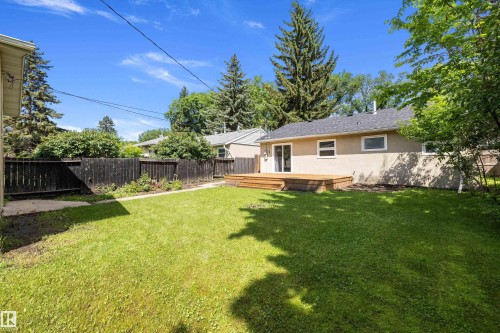 Expansive grassy backyard featuring a wooden deck, dark wood fencing, and mature trees - 12912 103 Street, Edmonton, AB 